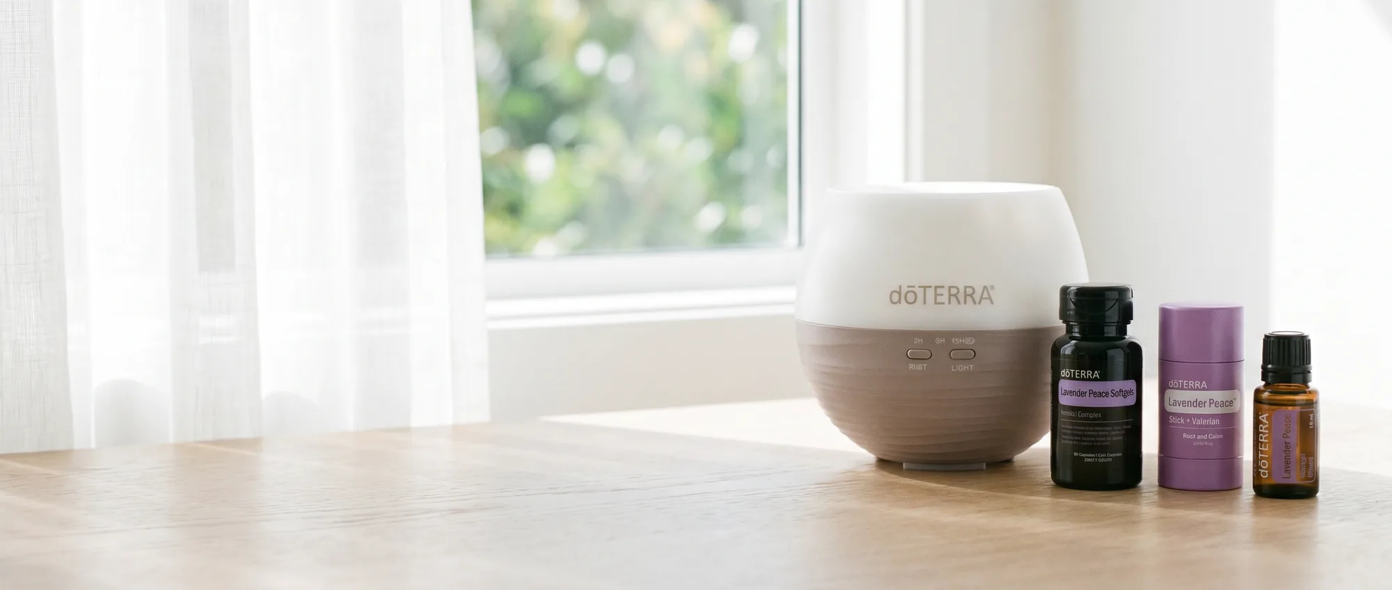 The dōTERRA Petal Diffuser, Lavender Peace Softgels, Lavender Peace Stick and Lavender oil in bright daylight on a timber tabletop