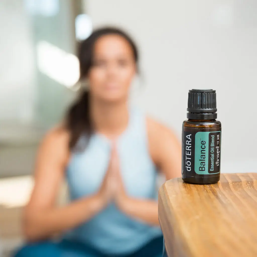 dōTERRA Essential Blends – a bottle of dōTERRA Balance essential oil in focus, with a woman meditating in the background, promoting relaxation and well-being.