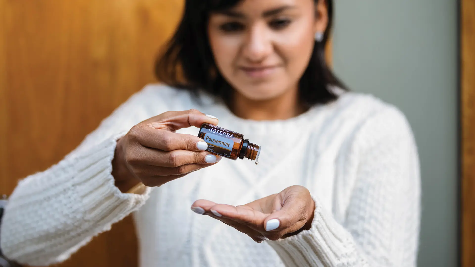 Woman applying dōTERRA Peppermint Oil into her hand from a 15 mL bottle, showing a drop mid-fall.