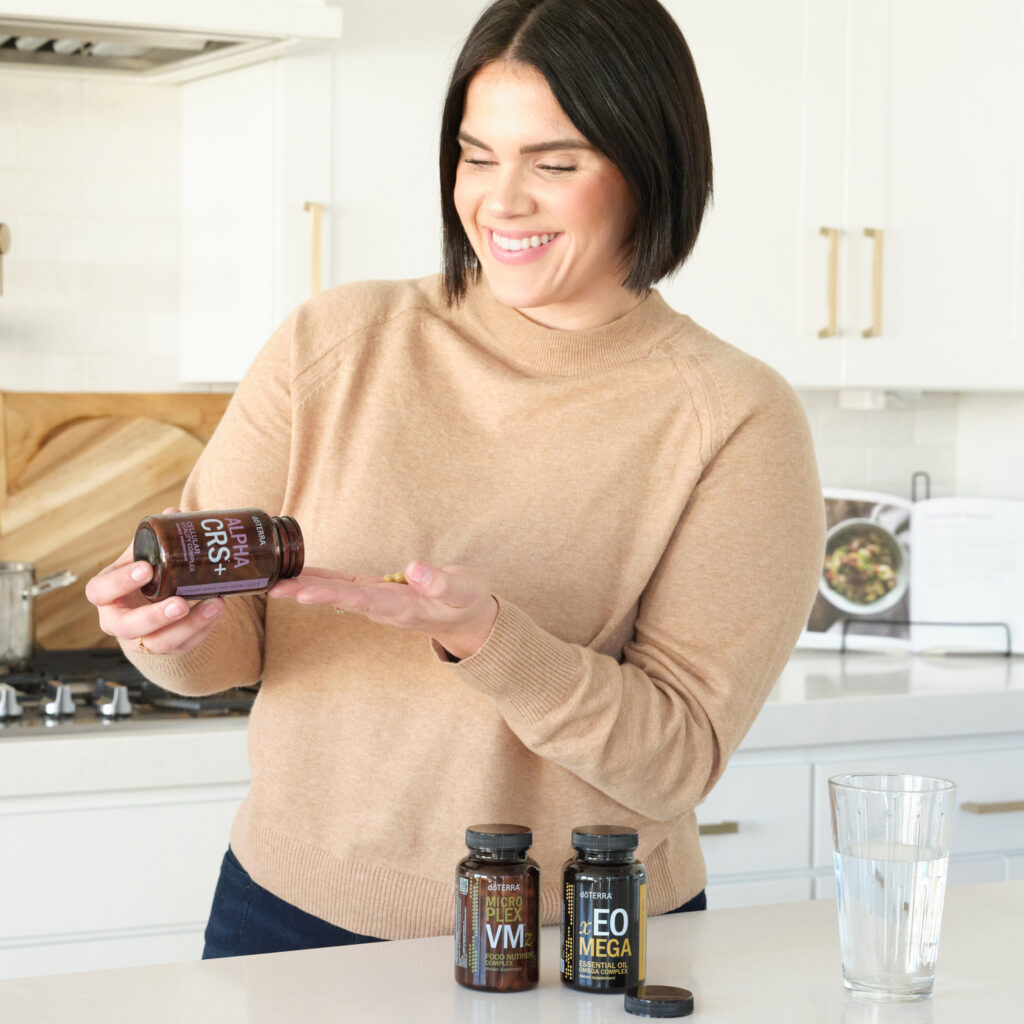 dōTERRA Supplements – a woman taking dōTERRA Lifelong Vitality supplements in a bright kitchen, supporting daily nutrition and wellness.