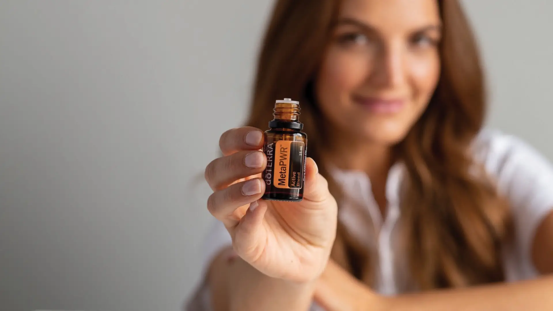 A woman holding up a bottle of dōTERRA MetaPWR Active Blend, showcasing its natural support for weight and energy balance.