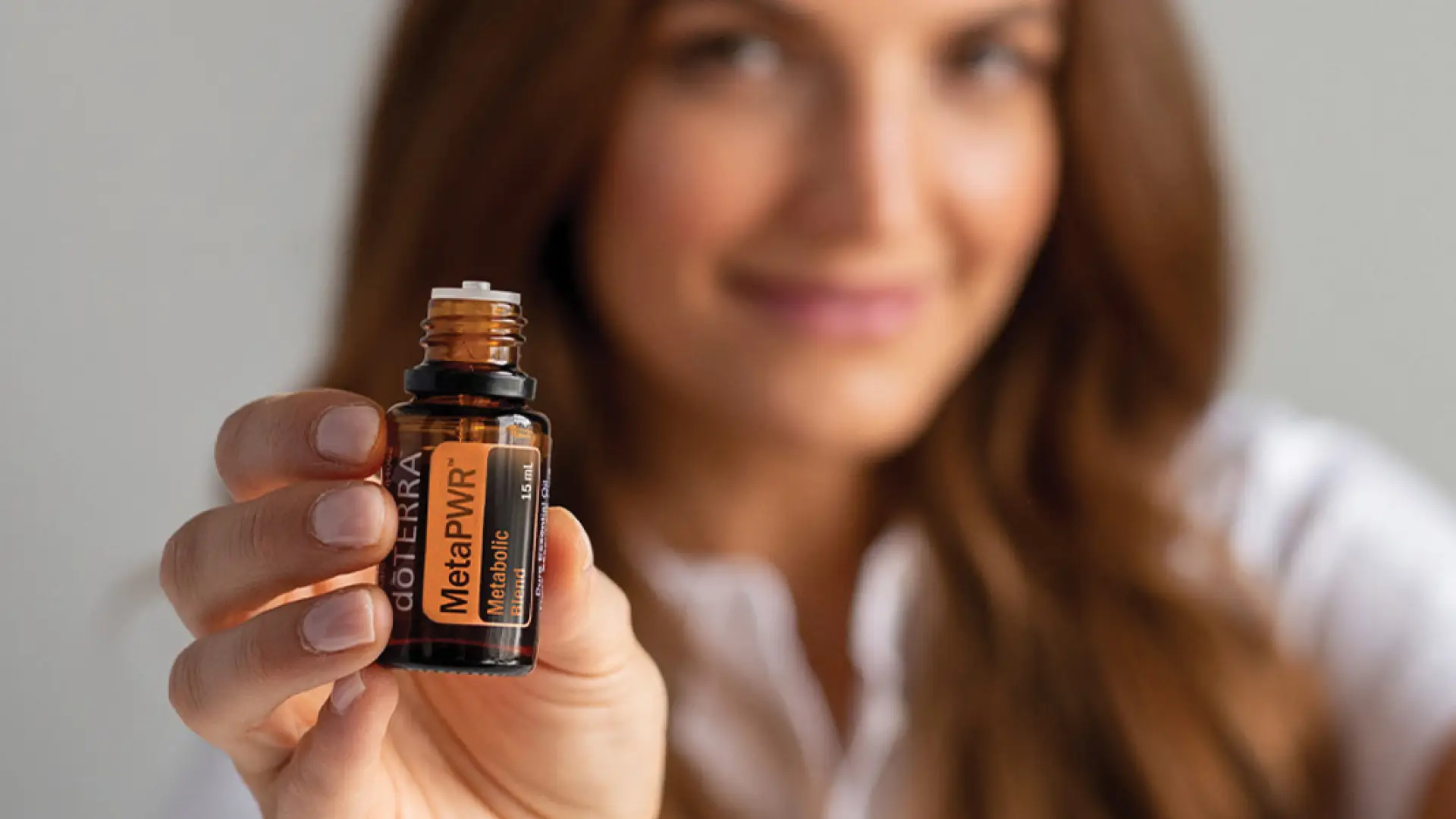 A woman holding up a bottle of dōTERRA MetaPWR Metabolic Blend, showcasing its natural support for weight and energy balance.